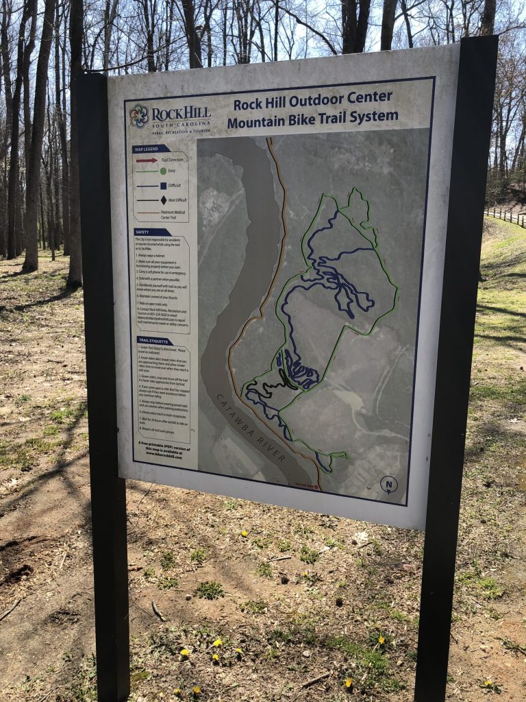 A weathered trail map sign greets visitors to the Rock Hill Outdoor Center, a popular mountain biking destination along the Riverwalk in South Carolina.