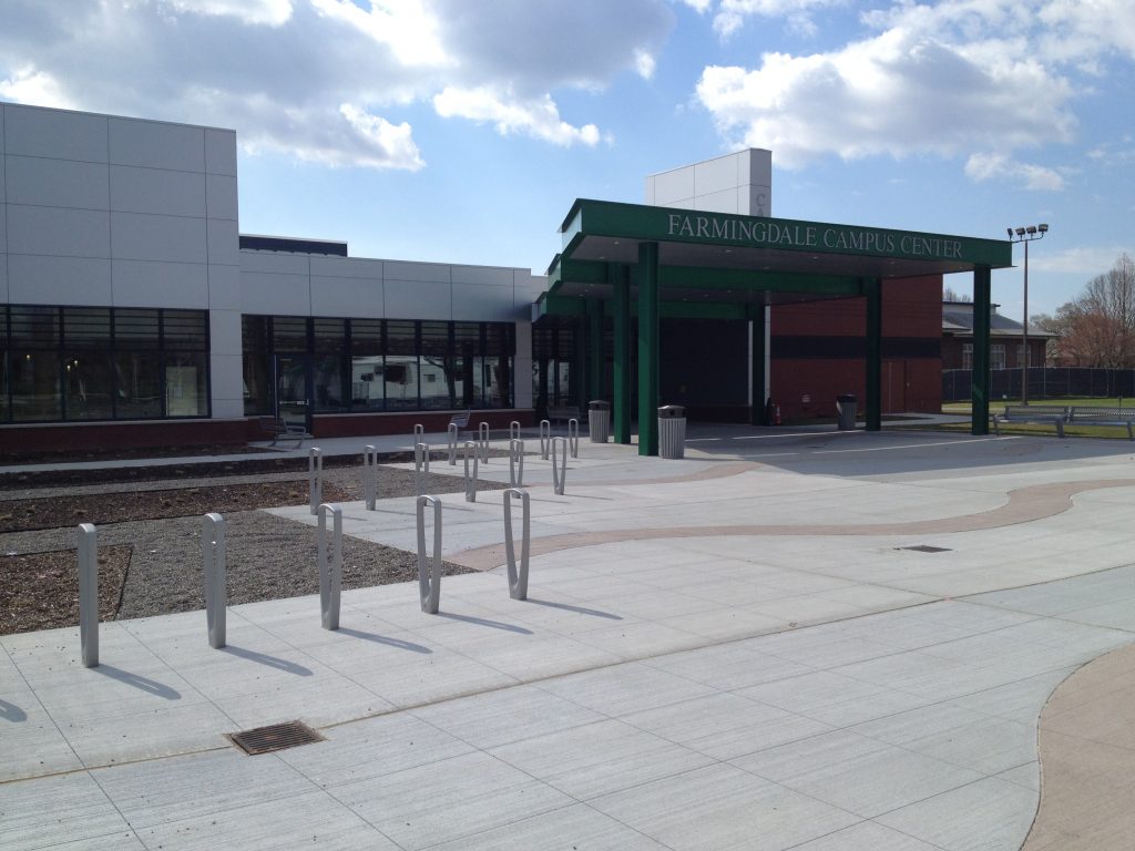 The Farmingdale Campus Center building with its green canopy entrance, glass facade, and rows of bike racks in front.