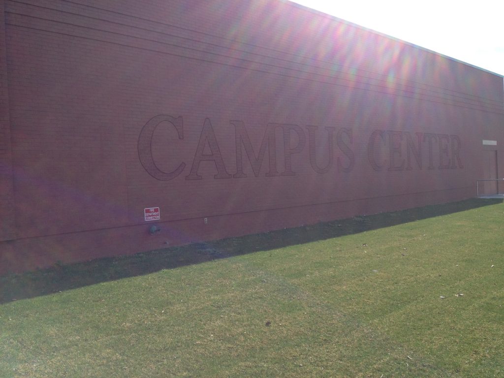 Large embossed letters spelling CAMPUS CENTER on a brick wall, with sunlight raking across the surface.