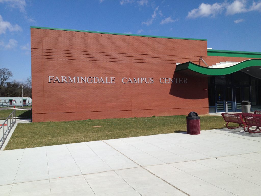 FARMINGDALE CAMPUS CENTER metal lettering on a brick wall beside a green wave canopy and outdoor benches.