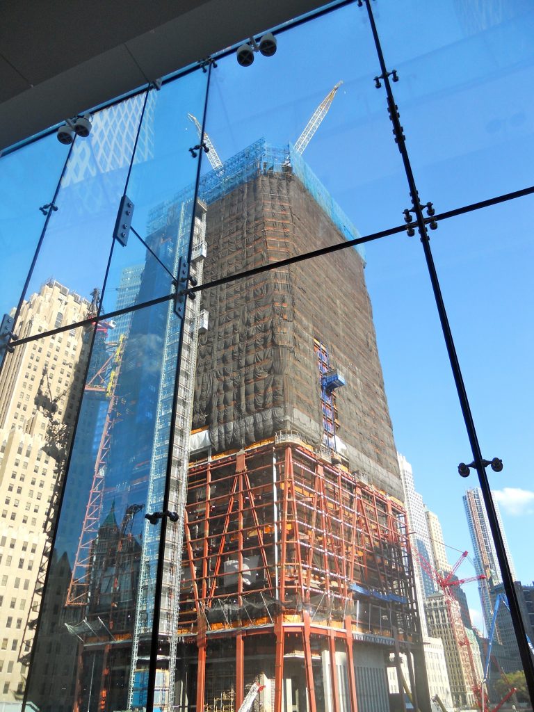 One World Trade Center construction tower seen through a glass viewing wall, showing the crane at the top and orange scaffolding at the base