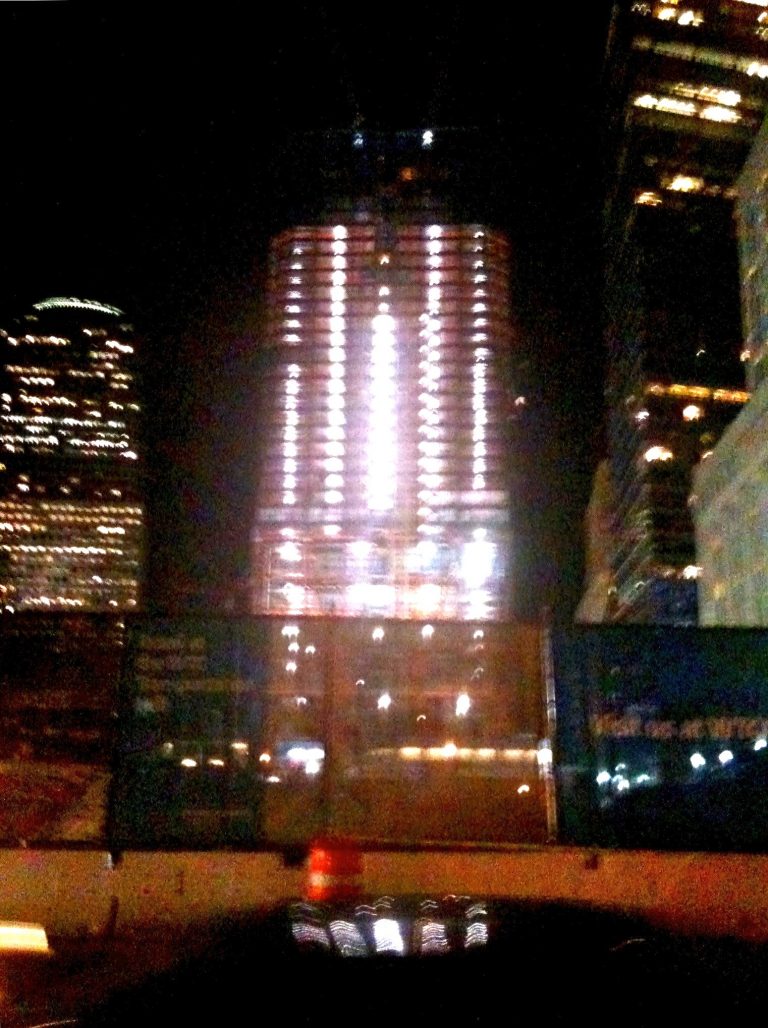 One World Trade Center towers above Lower Manhattan, ablaze with lights against the night sky.