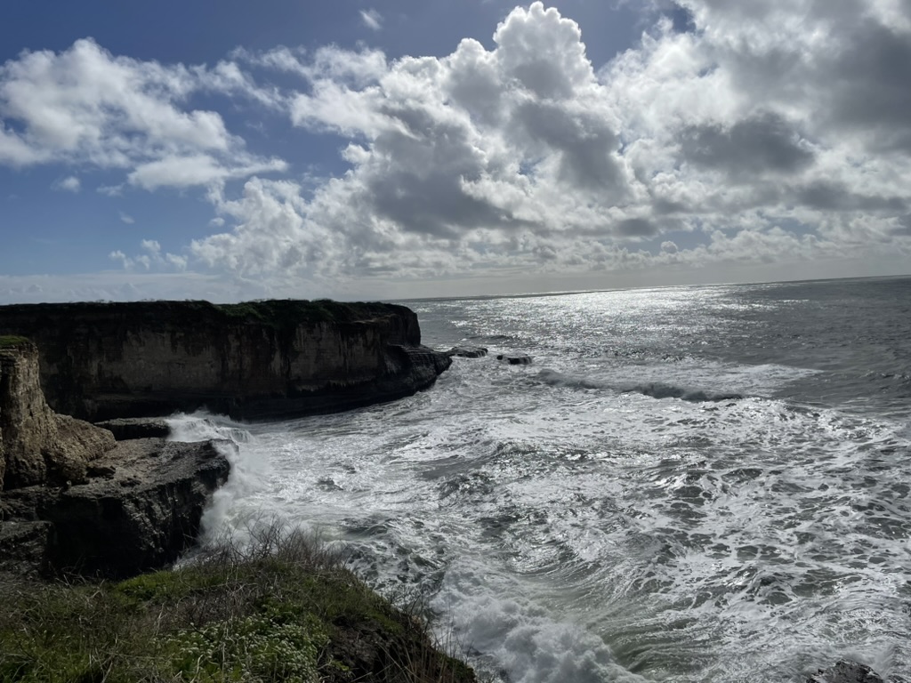 Rocky coastal cliffs and crashing waves under a cloudy sky