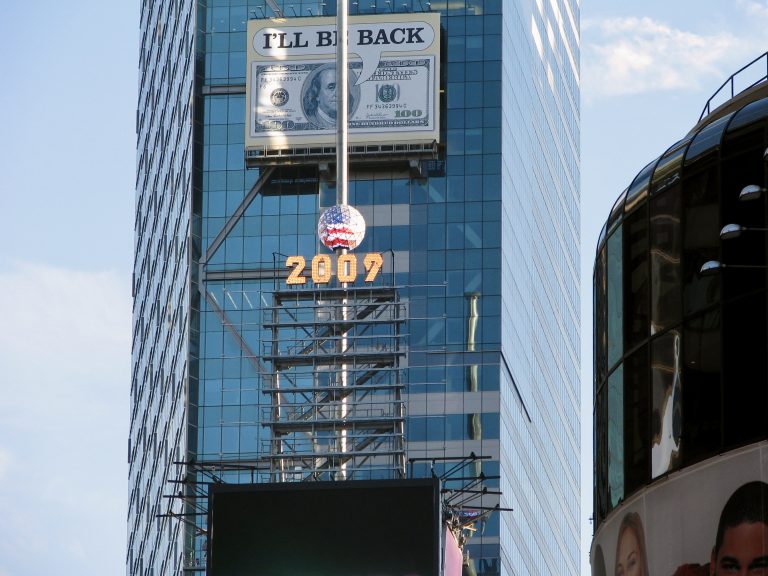The iconic Times Square New Year's Eve ball, marked with "2009," sits atop One Times Square alongside a giant $100 bill advertisement, captured during the July 4th 2009 weekend.