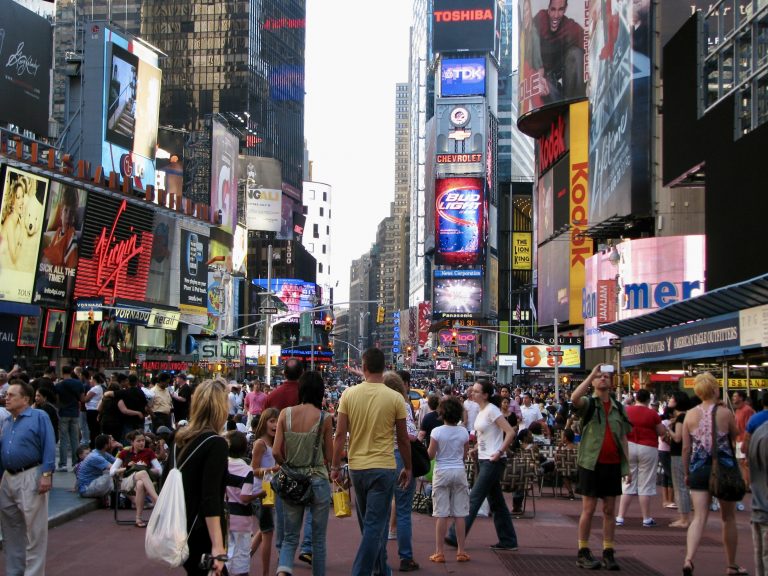 Massive crowds fill Times Square on July 4th, 2009, surrounded by iconic billboard advertisements from Toshiba, Chevrolet, Bud Light, and Kodak.