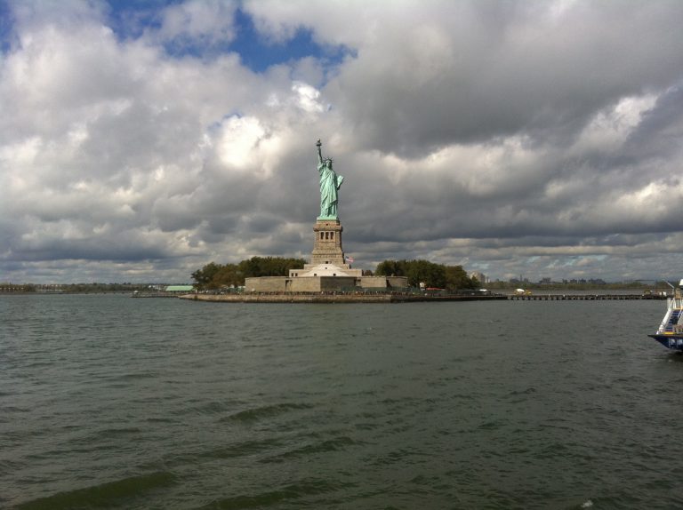 The Statue of Liberty stands on Liberty Island beneath a dramatic cloudy sky.