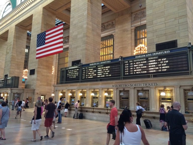 Travelers line up at the MTA Metro-North ticket windows beneath the Harlem Line departure boards.