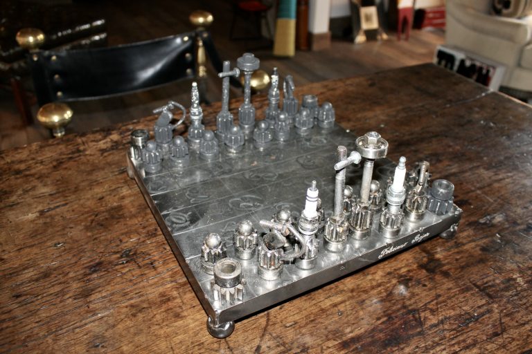 An industrial, hand-crafted chess set with pieces sculpted from spark plugs, bolts, and machine hardware on an engraved metal board. Wouldn't you prefer a nice game of chess?