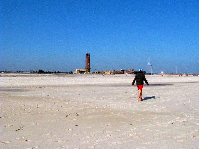 A solitary walker crosses the snow-dusted winter sand at Jones Beach.