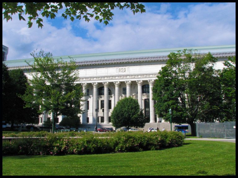 A wide view of the New York State Education Building's grand colonnade, framed by surrounding greenery.