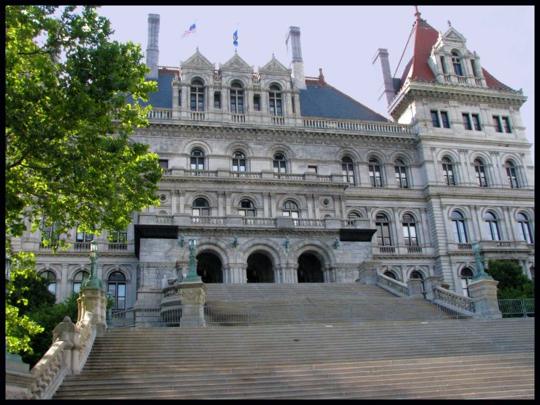 The grand front facade of the New York State Capitol, with its sweeping staircase and elaborate stonework.
