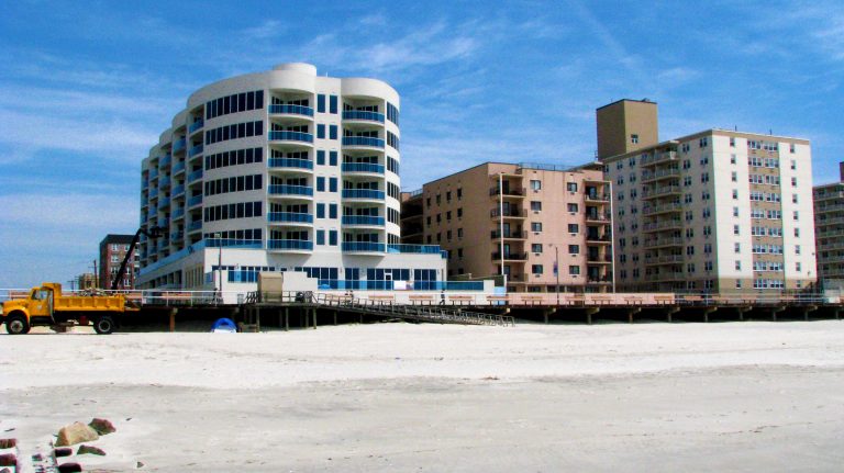 A new beachfront condo rises beside older brick towers.