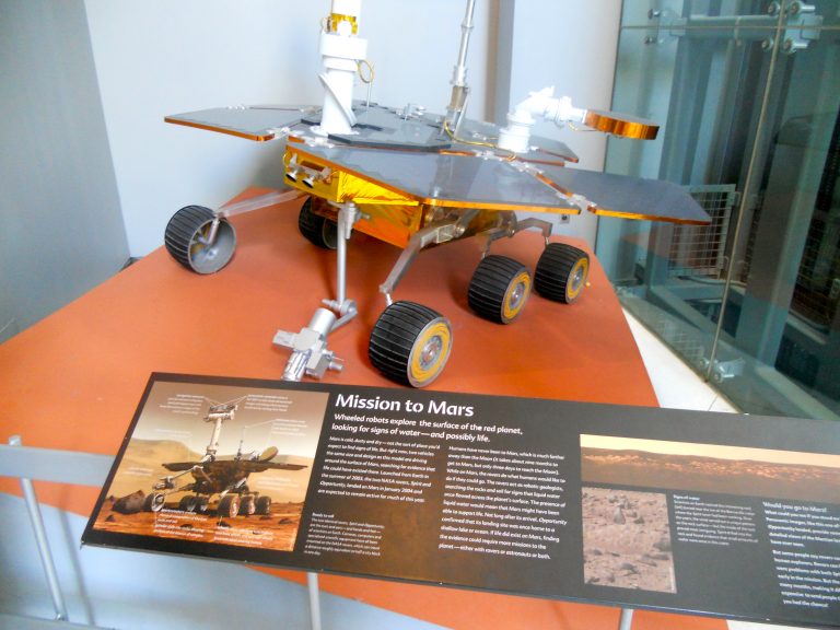 A detailed model of a Mars Rover on display at the American Museum of Natural History, alongside informational panels about the Mission to Mars.